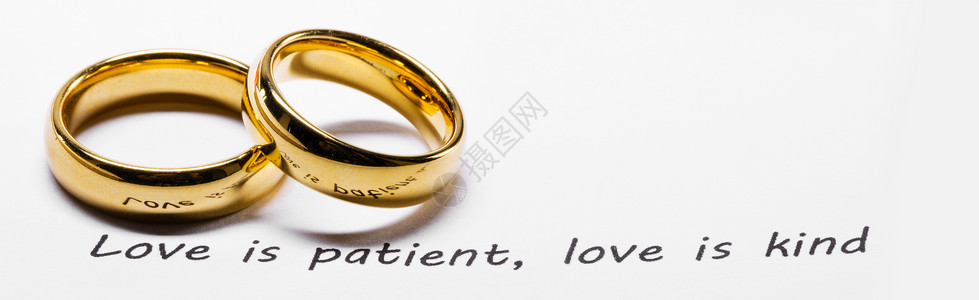 两个金色的结婚戒指圣经书上的短语特写,爱耐心的,爱善良的圣经短语上的金色结婚戒指背景图片