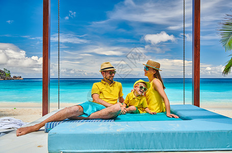 日光浴床家庭美丽的娇小的Anse海滩,穿着黄色衣服的年轻夫妇三岁的蹒跚学步的男孩马赛尔的暑假背景