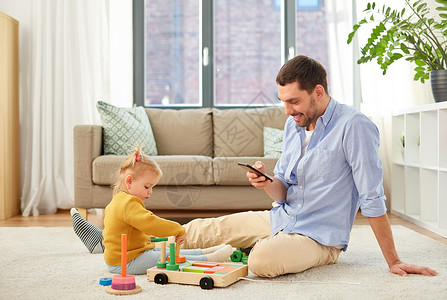 家庭,父亲人的快乐的父亲与智能手机小婴儿女儿玩木制玩具积木套件家里父亲带着智能手机女儿家背景图片
