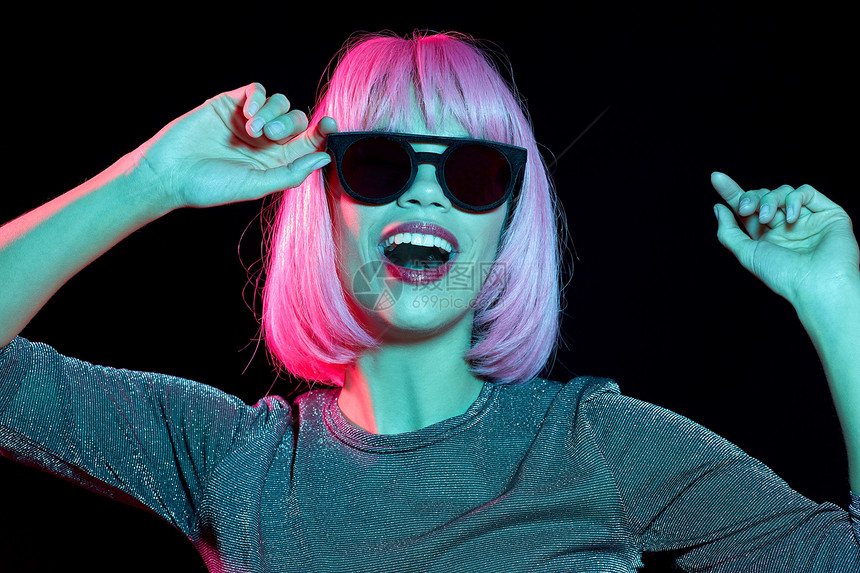 风格,时尚夜生活的快乐的年轻女人戴着粉红色的假发黑色霓虹灯的黑暗背景穿着粉红色假发黑色太阳镜的快乐女人图片