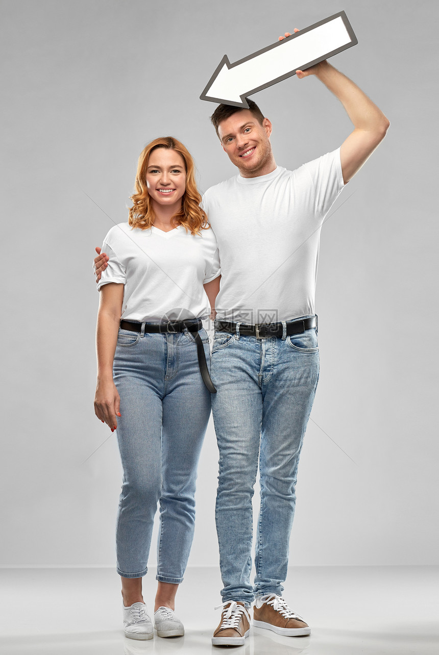 人际关系人的幸福的夫妇穿着白色T恤,灰色背景上向左伸出厚厚的箭头幸福的夫妇穿着白色T恤,左边有箭头图片