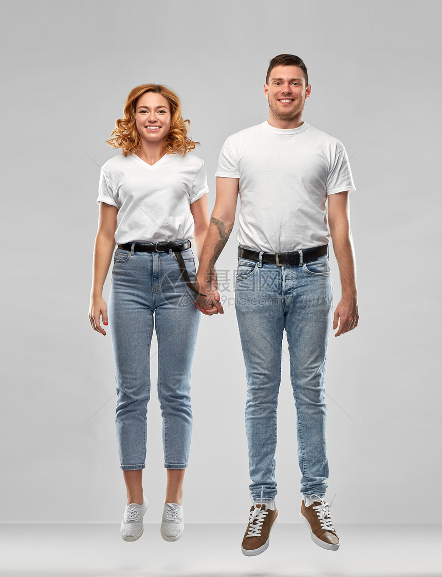 人际关系人的幸福的夫妇穿着白色T恤牵着手,灰色背景下跳跃或悬挂空中穿着白色T恤的幸福夫妇跳或挂图片