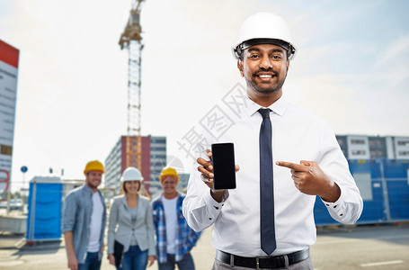 印度男人建筑,建筑业务人的微笑的印度男建筑师头盔智能手机建筑现场背景建筑师建筑工地展示智能手机设计图片