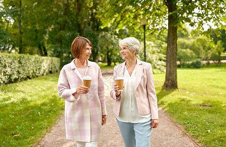 桃花散步喝饮料老年退休人的两个高级妇女或朋友公园喝咖啡散步交谈高级妇女或朋友公园喝咖啡背景