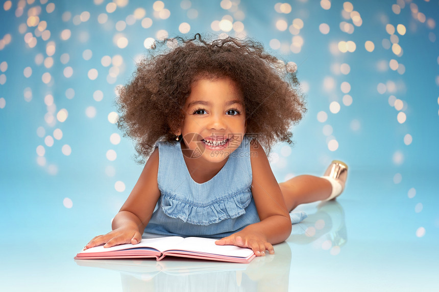 童年,学校教育快乐微笑的非裔美国女孩阅读书节日灯蓝色背景微笑的非裔美国女孩看书图片