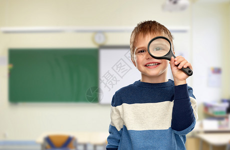 学校教育学理念微笑的小男孩透过放大镜看着教室的背景男孩学校看放大镜图片