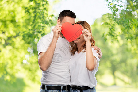 爱,情人节人际关系的微笑的夫妇躲红色的大心脏后面绿色的自然背景微笑的夫妇躲大红的心后面背景图片