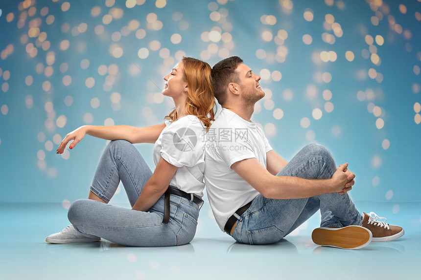 关系,风格人的幸福的夫妇穿着白色T恤坐地板上的灯光蓝色背景穿着白色T恤的幸福夫妇坐地板上图片