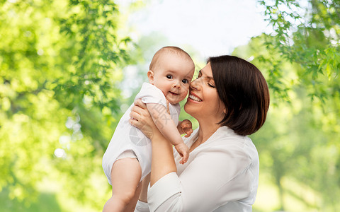 家庭,孩子父母的快乐的微笑中年母亲抱着小宝贝女儿绿色的自然背景快乐的中年母亲小女儿图片