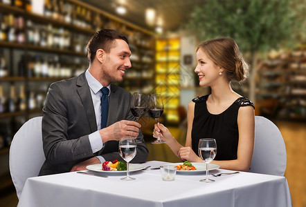 休闲奢侈的微笑的夫妇与食物叮当的红酒杯餐厅的背景微笑的夫妇餐厅碰杯图片