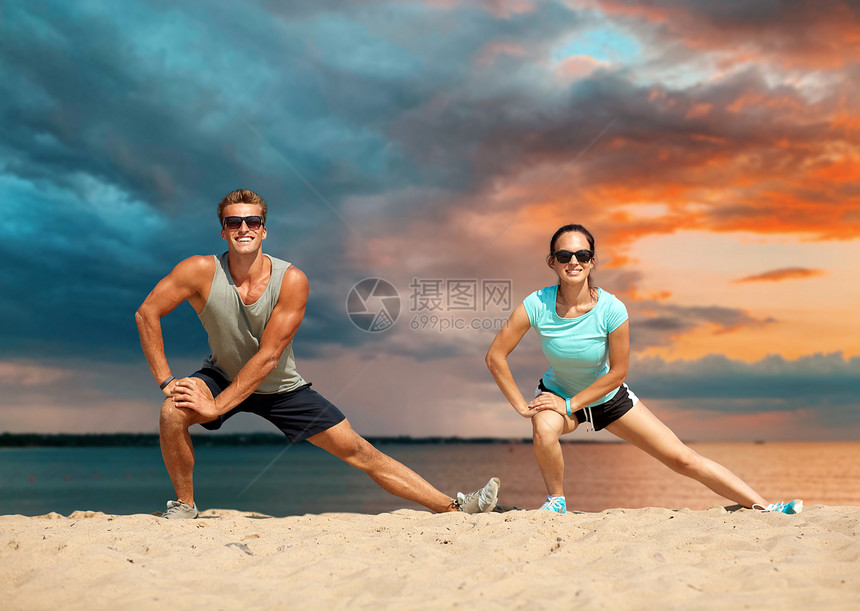 健身,运动生活方式的微笑的夫妇伸展腿海滩上,然后训练海上日落天空的背景微笑的情侣海滩上伸展腿图片