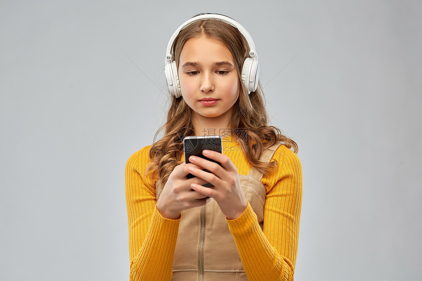 音频设备技术人员的十几岁的女孩耳机听音乐智能手机灰色背景戴耳机听音乐的十几岁女孩图片