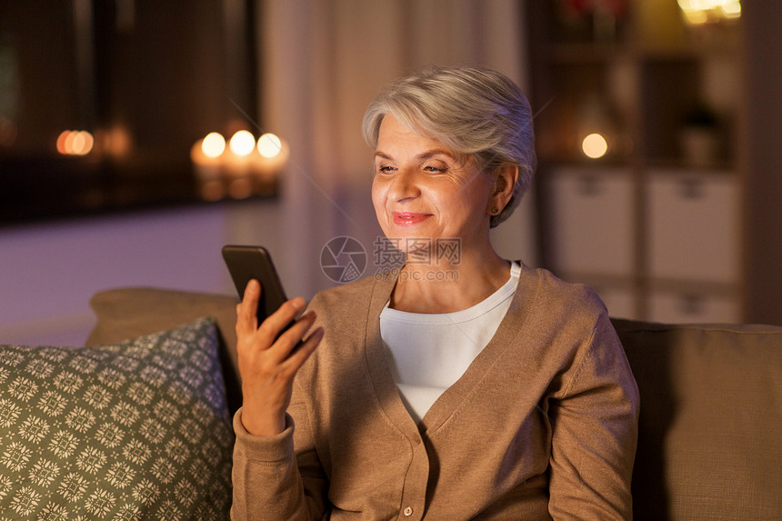 技术,沟通人的快乐的高级妇女与智能手机家里晚上快乐的高级女人家里有智能手机图片