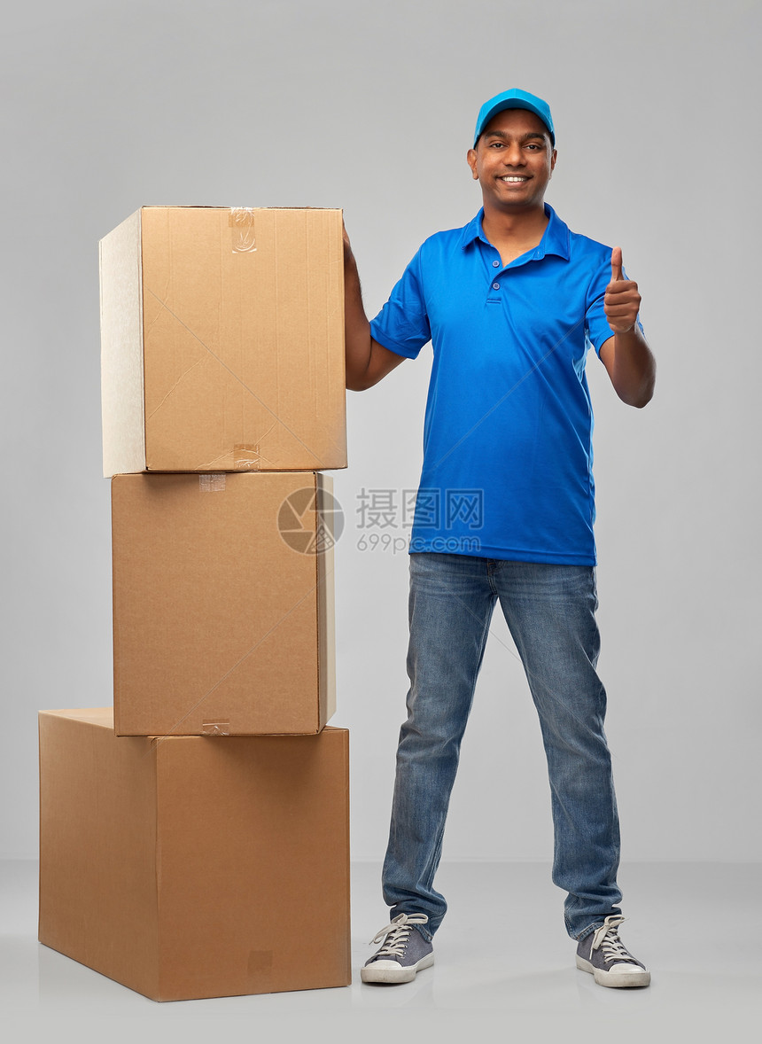 邮件服务装运快乐的印度送货人与包裹箱蓝色制服灰色背景快乐的印度送货人带着包裹箱图片
