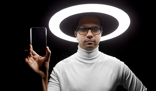 印度男人未来的技术虚拟现实印度男子戴着透明智能手机的眼镜,黑色背景下白色照明戴眼镜的男人照明下戴着智能手机设计图片