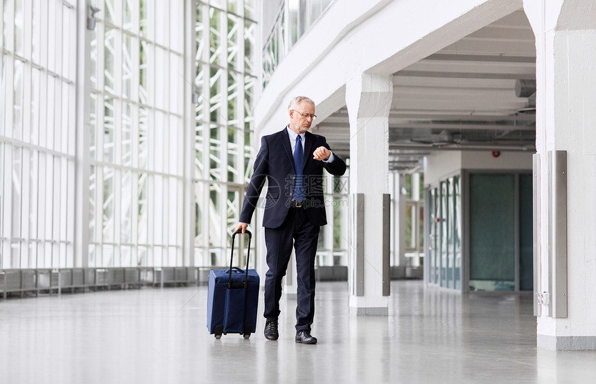 商务旅行,公司人的资深商人带着旅行袋沿着办公楼或机场步行检查时间资深商人带着旅行袋走路图片