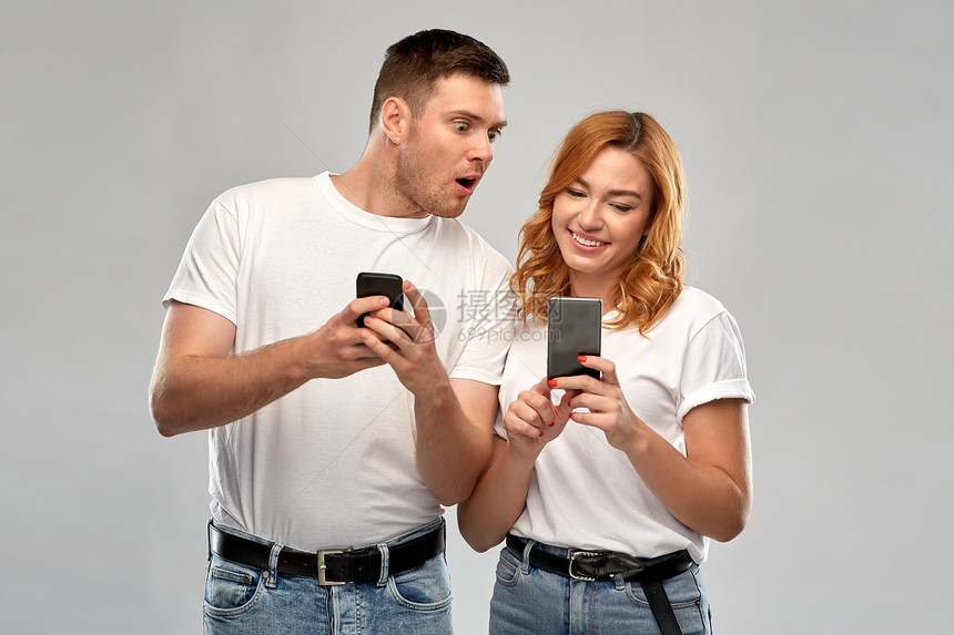 技术人的幸福的夫妇穿着白色T恤与智能手机灰色背景穿着白色T恤智能手机的幸福夫妇图片
