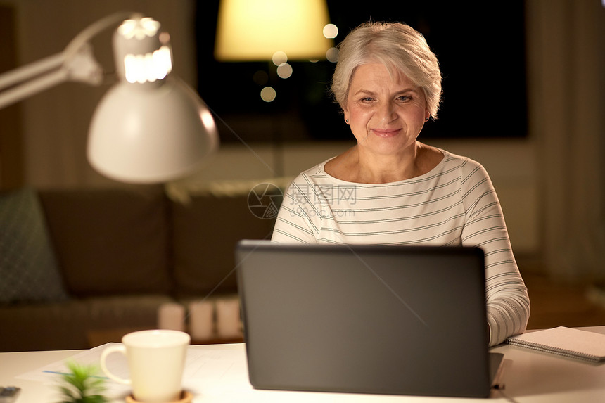 技术,老年人人的快乐的老年妇女家里的笔记本电脑晚上快乐的高级女人晚上家带笔记本电脑图片