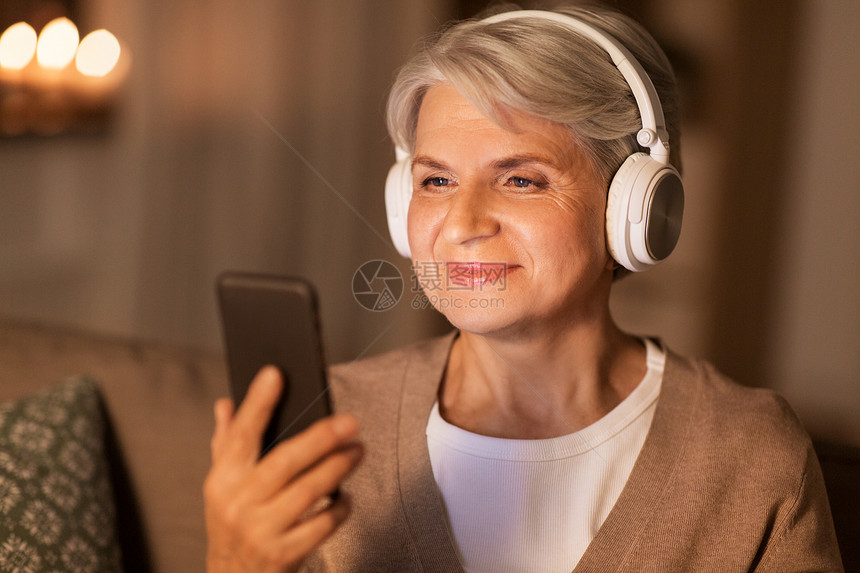 技术,人生活方式的快乐的高级妇女耳机听音乐智能手机家里晚上戴耳机听音乐的高级女人图片