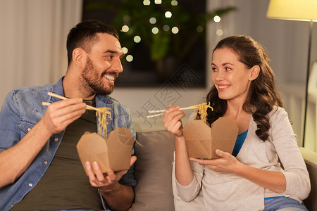 快餐人们的快乐的夫妇晚上家吃带筷子的外卖面条幸福的家里吃外卖面条图片