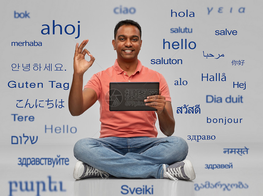 技术,沟通人的快乐的印度男人,平板电脑坐地板上,灰色背景下用同的外语问候语快乐的印度男人与平板电脑图片