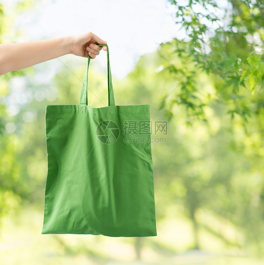 消费主义生态友好的手可重复用的帆布袋,用于绿色自然背景下的食品购物手持可重复用的帆布袋进行食品购物图片