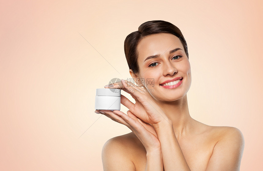 美丽,化妆品护肤品的快乐的年轻女人着罐奶油米色背景快乐的年轻女人着罐奶油图片