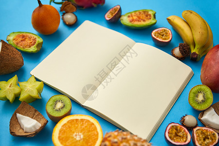 纳迪食物,饮食健康饮食同的异国水果围绕笔记本或日记,空页蓝色背景带空页的笔记本周围的异国水果背景