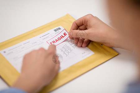易碎标志素材送货邮件服务人员装运妇女的手邮局的信封上贴着易碎的标记把易碎的痕迹粘信封里的包裹上背景