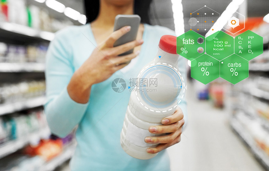 饮食,技术人的年轻妇女与智能手机持有奶瓶杂货店或超市的食物营养价值图表有智能手机的女人超市买牛奶图片