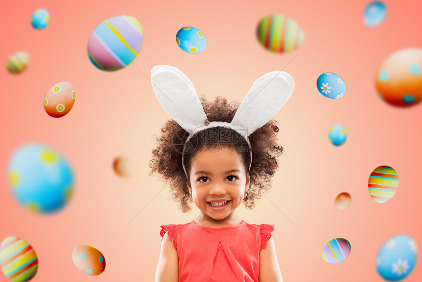 复活节,假期童年的快乐的非裔美国女孩戴着兔子耳朵,头带活生生的珊瑚背景彩色鸡蛋上快乐的小女孩戴着复活节兔子的耳朵图片