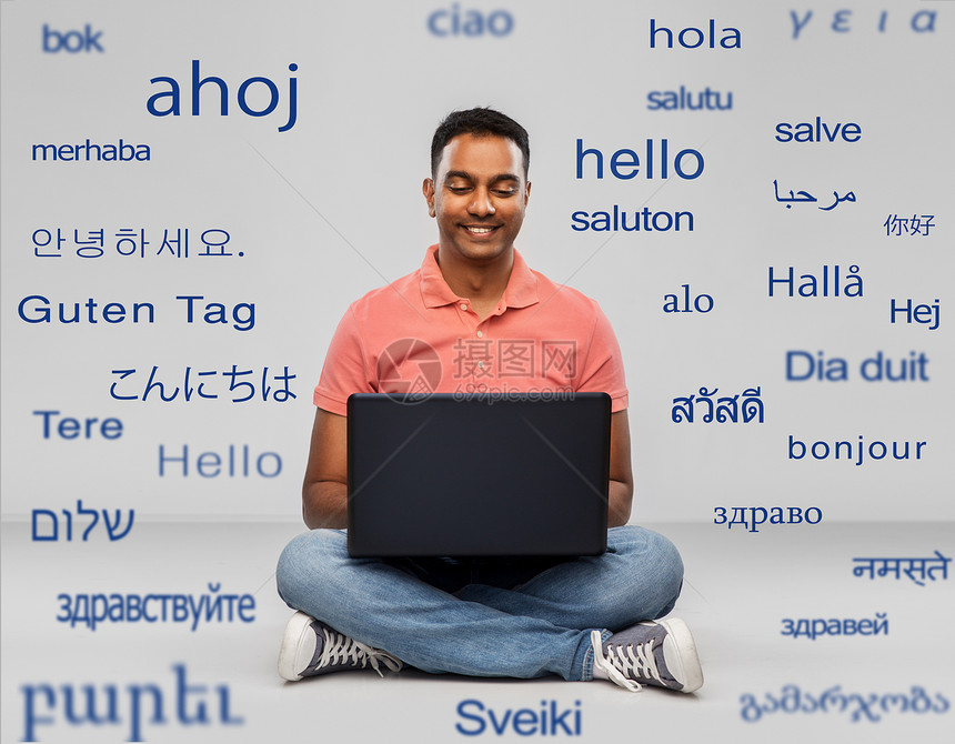 技术,沟通人的快乐的印度男人,笔记本电脑坐地板上,灰色背景下用同的外语问候语快乐的印度男人,地上有笔记本电脑图片