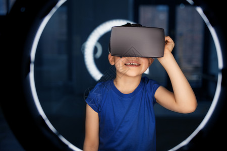 圆眼镜未来的技术人们的快乐的微笑男孩VR眼镜或虚拟现实耳机白色照明黑暗的房间男孩戴着VR眼镜,黑暗的房间里照明背景