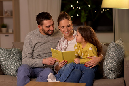 家庭休闲人的快乐的父亲母亲小女儿晚上家看书晚上家快乐的家庭读物图片