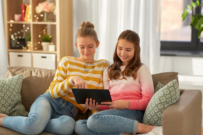 人,技术友谊的快乐的少女与平板电脑坐沙发上家快乐的女孩与平板电脑坐沙发上家图片