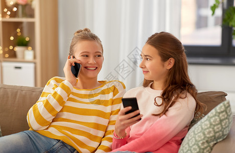 家里有矿人,技术友谊的快乐的十几岁的女孩坐沙发上的智能手机家快乐的十几岁的女孩家里有智能手机背景