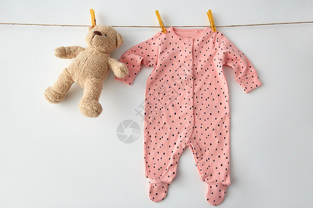 衣服,洗衣,婴儿期服装粉红色长袖西装为女婴与点打印挂晾衣绳与泰迪熊别针白色背景小女孩用泰迪挂绳子上的紧身衣背景图片