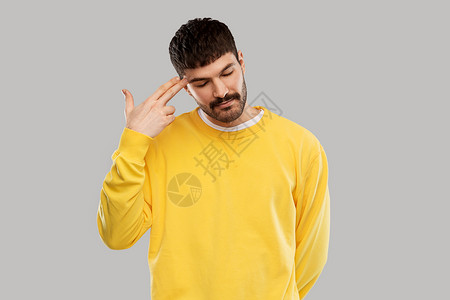 人,表情压力的无聊的年轻人穿着黄色运动衫,用手指的手势头部射击无聊的人做手指的手势背景图片