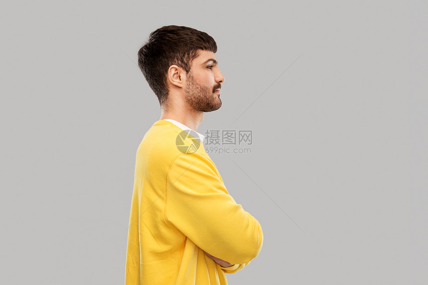 人们的年轻人穿着黄色运动衫,双臂交叉灰色背景上穿着黄色运动衫的年轻人交叉手臂图片