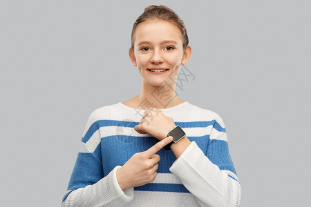 技术人的快乐的微笑少女套衫与智能手表灰色背景快乐微笑的十几岁女孩带着聪明的手表背景图片