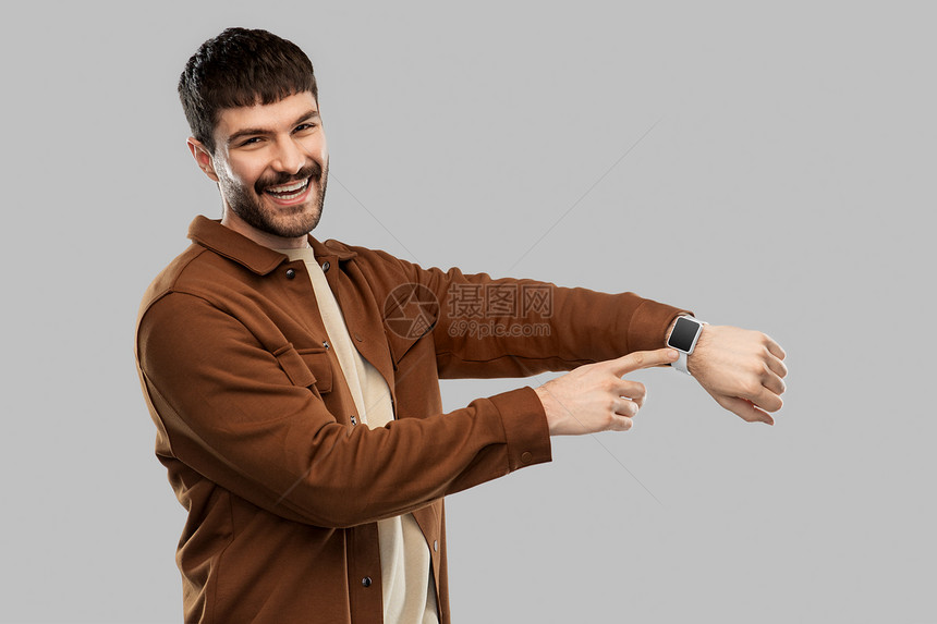 技术人的微笑的年轻人,聪明的手表灰色背景微笑的年轻人带着聪明的手表图片