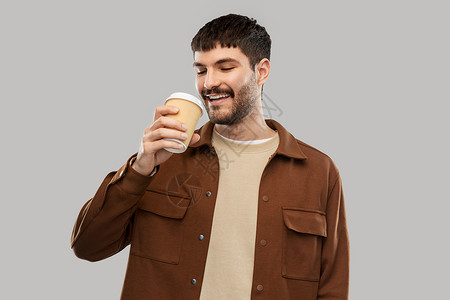 饮料人们的微笑的年轻人喝咖啡外卖杯灰色背景快乐的年轻人外卖杯里喝咖啡背景图片