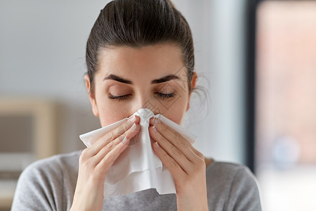 医疗保健,感冒,过敏人的密切生病的女人家里用纸巾吹鼻涕生病的女人家里用纸巾吹鼻子背景图片