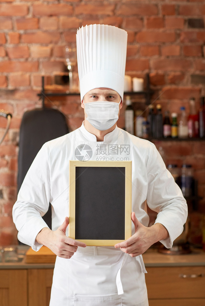 健康安全大流行男厨师或面包师戴着面部防护医学面具,以防止病疾病,餐厅厨房背景上用空白菜单粉笔板男厨师面罩图片