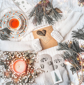 冬季圣诞之家白色针织毛衣上的信封,冬天的花环,有趣的温暖的小猫袜子,冷杉树枝,燃烧的蜡烛,波克,杯茶带雪花的智能手机背景图片