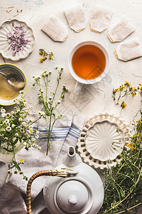 杯带茶袋的凉茶,茶壶,白色桌子上有新鲜的草药蜂蜜,顶部风景健康的生活方式图片