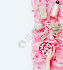 女手水碗,粉红色毛巾上有鲜花,有各种环保的护肤美容工具白色背景上的刷子海绵浮石化妆品上面的风景平躺背景图片