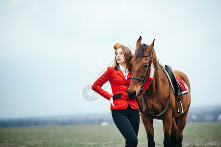 红发骑师女孩穿着红色开衫黑色高靴,带着匹马散步背景图片