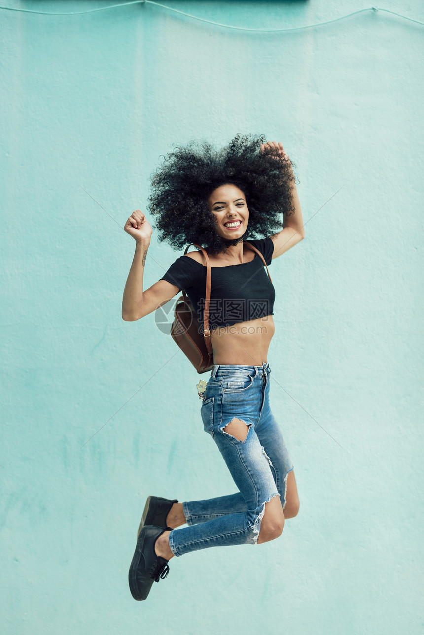 年轻的混血女人,头发户外跳跃女穿着休闲服装城市背景生活方式的图片