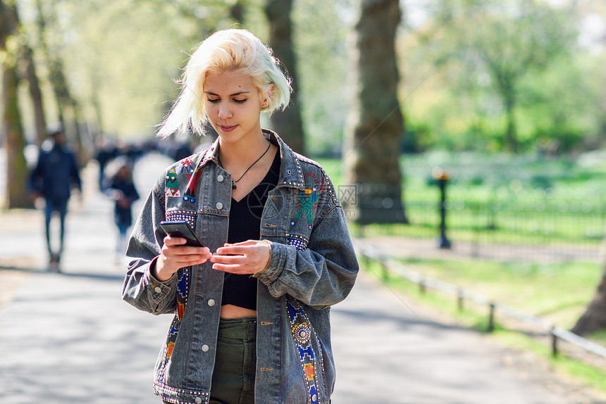 年轻的城市女,现代发型,用智能手机伦敦的个城市公园的街道上行走年轻的城市女,用智能手机城市公园的街道上图片